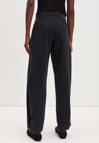 Hochtaillierte, weit geschnittene schwarze Jeans aus Denim mit aufgesetzten Taschen und umgeschlagenen Säumen, die eine Stofftextur aufweisen, die weich und gleichzeitig robust wirkt.