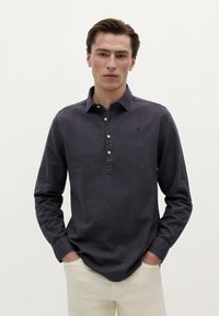 Donker marineblauwe langarmshirt met knopenlijst en kraag. De stof heeft een gladde textuur en bevat een klein logo-accent.