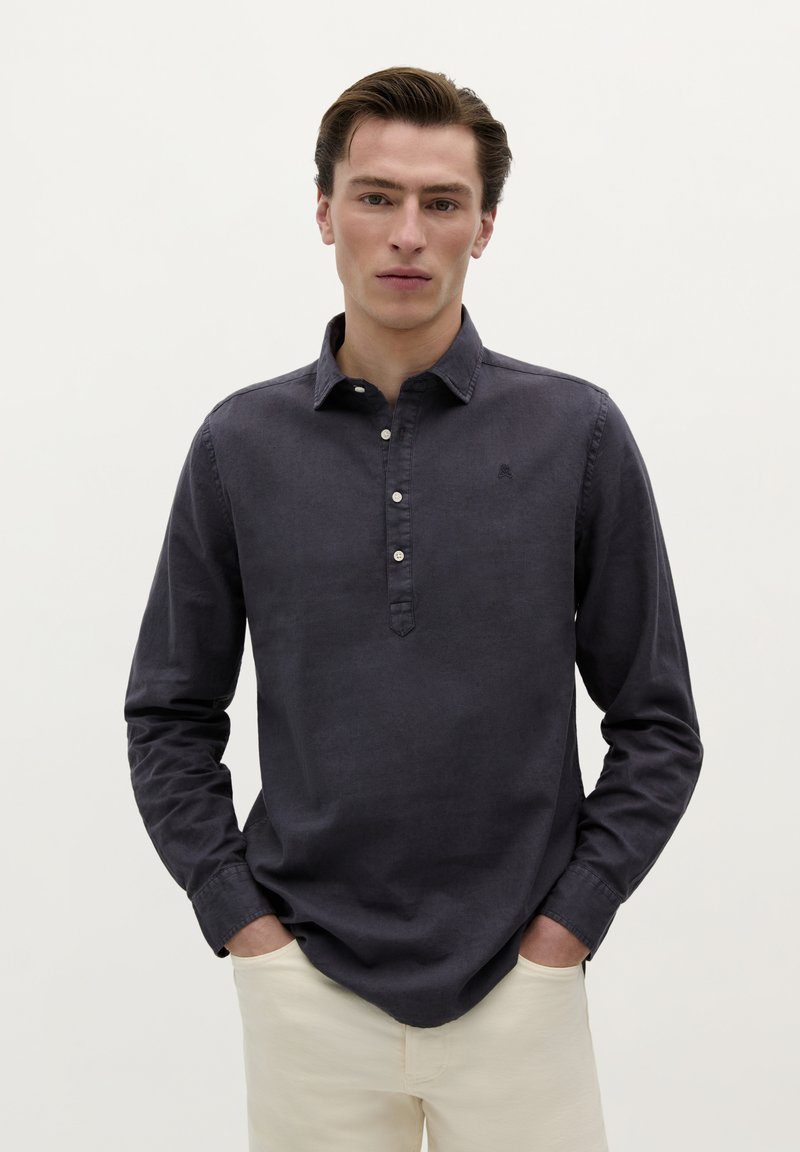 Donker marineblauwe langarmshirt met knopenlijst en kraag. De stof heeft een gladde textuur en bevat een klein logo-accent.