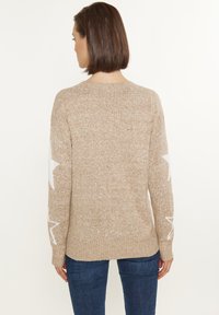Beige kötött pulóver hosszú ujjakkal, fehér csillagmintákkal az ujjakon. Bordázott mandzsetták és alj, puha, texturált anyagból készült.