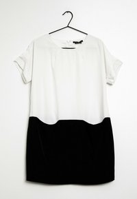 Lyhythihainen mekko, jossa on valkoinen yläosa ja musta hameosa. Sileä kangas, pyöreä pääntie ja käännettävän hihan yksityiskohta. Roikkuu mustassa koukussa.