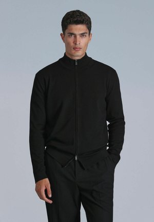 Zwarte zip-up jas van gebreid materiaal met een hoge kraag, met een tweezijdige rits aan de onderkant en aansluitende lange mouwen.