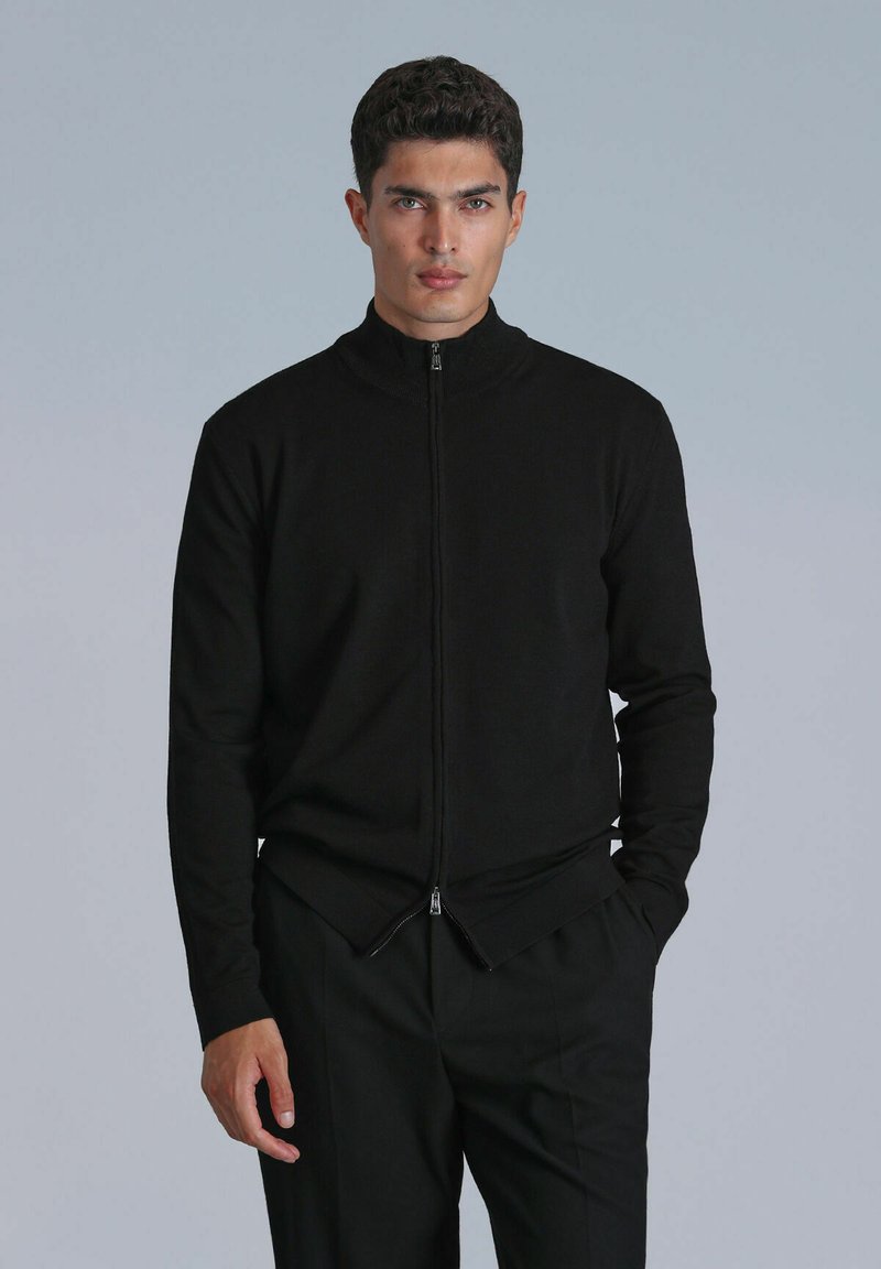 Zwarte zip-up jas van gebreid materiaal met een hoge kraag, met een tweezijdige rits aan de onderkant en aansluitende lange mouwen.
