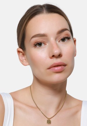 Collier en chaîne torsadée en or avec un pendentif carré à la texture travaillée. Modèle à la peau claire et au maquillage neutre sur fond blanc.