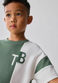 Grøn og hvid farveblokeret T-shirt med korte ærmer, med et logo "TB BAKER" i mørkegrøn på brystet. Blødt bomuldsmateriale.