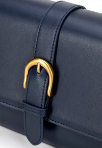 Marineblaue Lederhandtasche mit strukturierten Oberflächen, ausgestattet mit einem goldenen Schnallendetail und einem genähten Tragegurt. Kompakte rechteckige Form.