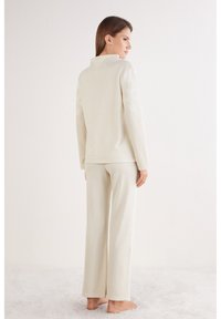 Lounge set in crèmekleur met een coltrui en wijde broek. Zachte textuur met subtiele sneeuwvlokpatronen op de mouwen.