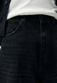 Mustat farkut korkealla vyötäröllä, viisitieleitä ja hienovaraiset kulutukset etutaskun reunassa.