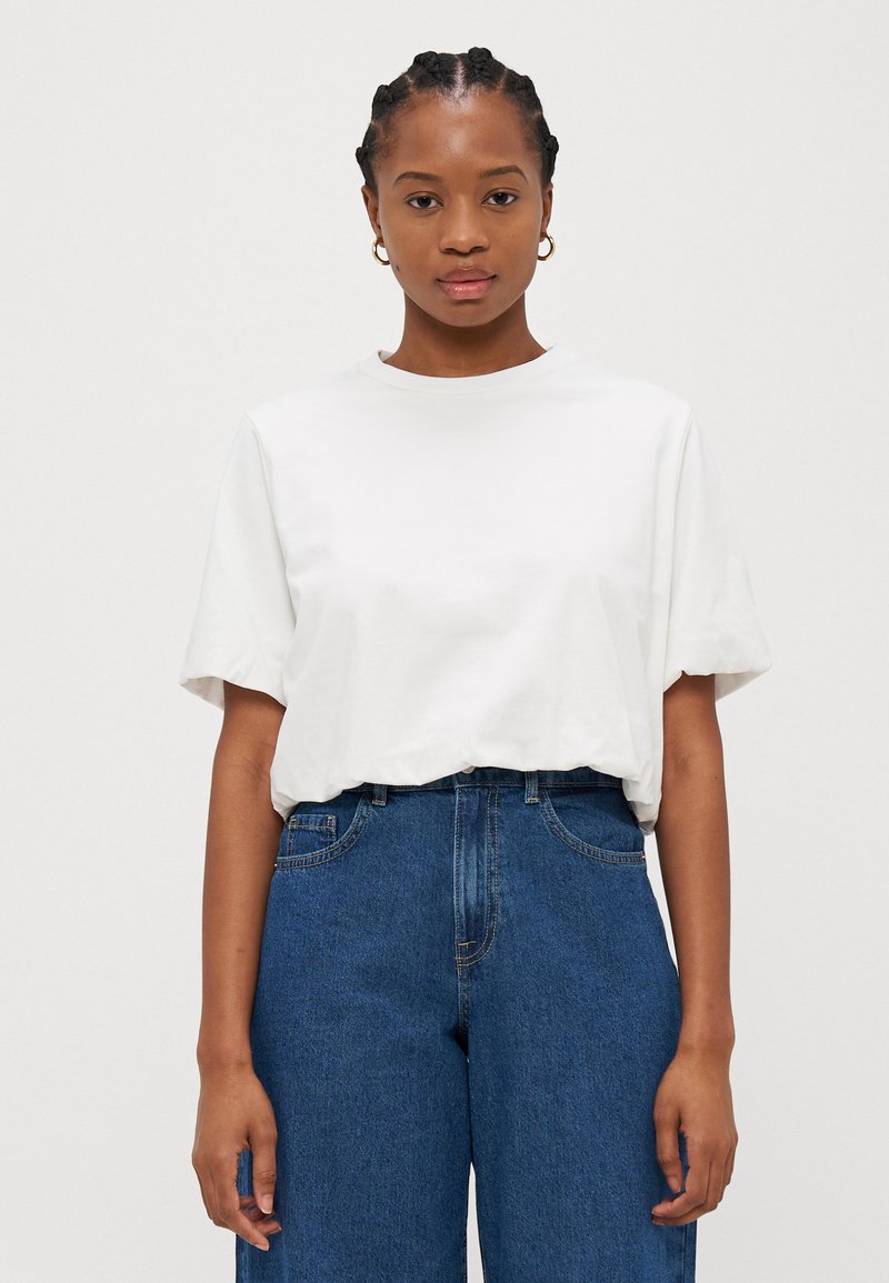 White cotton t-shirt with short sleeves, round neck, and relaxed fit, paired with high-waisted blue denim jeans. Smooth texture, no visible patterns.