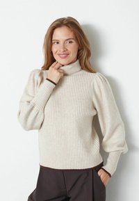 Maglione a collo alto rigato beige chiaro con maniche a sbuffo e rifiniture marroni. Texture morbida e design aderente con una vestibilità leggermente rilassata sui fianchi.