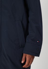 Mørkeblå vandtæt jakke med lynlås, sidelommer og manchetter med knap og en lille logoaccent. Glat tekstur.