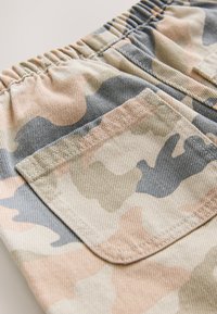 Shorts camouflage présentant un mélange de teintes beige, vert et gris. Taille élastique, avec une poche à rabat à l'arrière. Tissu texturé.