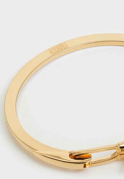 Χρυσής απόχρωσης βραχιόλι με λεία, γυαλιστερή επιφάνεια, που διαθέτει καμπυλωτό σχέδιο και ασφαλή μηχανισμό κλειδώματος. Χαραγμένες ενδείξεις μεγέθους στην εσωτερική πλευρά.