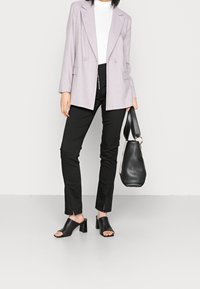Ljuslila blazer med dubbelknapdesign, vit turtleneck, svarta tighta byxor med sprund, svarta klackskor och en svart handväska.