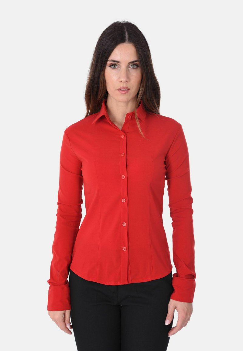 Camicia rossa a maniche lunghe con colletto, design aderente, texture liscia e bottoni abbinati. Indossata con pantaloni neri.