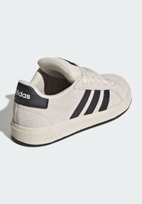 Adidas sneakers i ljusbeige mocka, med svarta läderdetaljer, tre svarta ränder och en strukturerad vit gummisula.