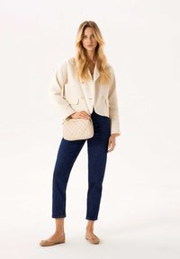 Giacca in tweed crema con due bottoni, jeans blu scuro, borsa trapuntata beige e ballerine beige su uno sfondo neutro.
