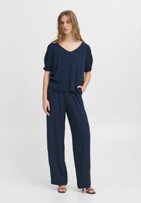 Námorně modrý dvoudílný outfit se voln�ým topem s V-výstřihem a širokými kalhotami, vyrobený z lehkého materiálu, s uvolněným střihem a jemnou texturou.