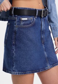 Donkerblauwe denimrok met een aansluitende taille, ceintuurlussen en zakken. Kenmerkende stiksels en een nette zoom zorgen voor een gestructureerde uitstraling.