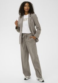 Costume gris à rayures avec un blazer ajusté et un pantalon à cordons assorti, superposé sur un t-shirt blanc avec "LIBERTÉ" en lettres dorées.