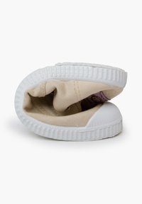 Scarpa di tela beige con parte superiore morbida, suola in gomma bianca e dettagli texture. La scarpa è mostrata piegata e rivoltata.