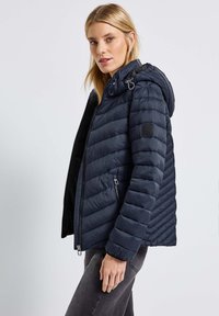 Veste doudoune marine avec capuche, dotée d'une fermeture éclair à l'avant, de poches zippées et d'un motif matelassé. Fabriquée en matériau synthétique lisse et léger.