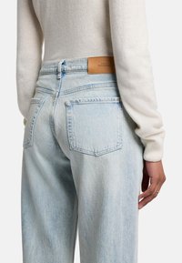 Jeans in denim blu chiaro con vita alta, due tasche posteriori e una patch in pelle sulla cintura. Tessuto morbido e vestibilità ampia.