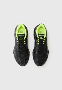Fekete fűzős sportcipők, textúrált műbőrből, élénk lime zöld részletekkel és gumitalppal, Lacoste logóval a nyelvén.