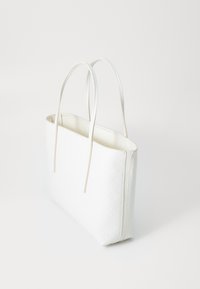 Borsa tote in pelle bianca con un sottile motivo geometrico, due manici lunghi e una parte superiore aperta, fotografata su uno sfondo bianco uniforme.