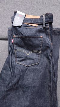 Jeans de denim azul escuro dobrados, mostrando o bolso traseiro com costura de assinatura e uma etiqueta e rótulo da marca Levi's na cintura.