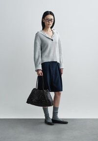 Grijze geribbelde trui met knoop, marineblauwe rok, donker gevlochten handtas, grijze sokken en zwarte ballerina's. Eenvoudige lijnen en texturen.