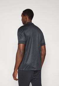 Fekete rövid ujjú galléros póló bordázott textúrával, finom részletekkel a gallérnál és testhezálló kialakítással atletikus viselethez.