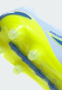 Gros plan sur la semelle jaune et bleue d'une chaussure de football à crampons coniques avec le texte « Powerspine » sur la plaque de soutien de la voûte plantaire.