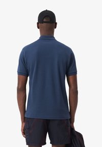Polo bleu marine à manches courtes et col. Le matériau semble doux et lisse. Porté avec un short foncé, montrant un design épuré.