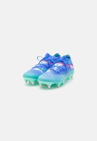 Scarpe da calcio blu brillante con accenti verdi, tomaia texturizzata, tacco rialzato e tacchetti bianchi. Presentano lacci blu e un design a motivo.