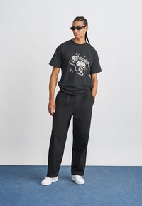 Svart grafisk t-skjorte med hvit design, kombinert med løse svarte bukser og hvite joggesko. Modellen har på seg sorte solbriller.