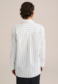 White long-sleeve shirt with black vertical stripes, featuring a collar, button cuffs, and a pleated back detail.