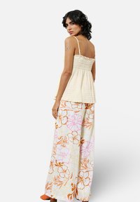 Lichtgele peplumtop met spaghettibandjes, voorzien van een textuurontwerp. Een paar wijde broek met bloemenpatronen in oranje en roze.