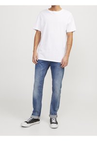 T-shirt en coton blanc avec un col rond, associé à un jean en denim bleu clair et des baskets noires avec des lacets blancs et une semelle en caoutchouc.