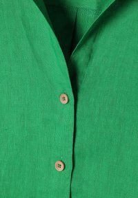 Green linen shirt featuring a V-neck design, a wooden button, and a textured surface, suitable for casual wear.