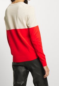 Svetr v červené a béžové barvě s dlouhými rukávy, kulatým výstřihem a žebrovanými manžetami. Měkká textura, přiléhavý střih.