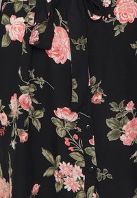 Blusa nera floreale con rose rosa e foglie verdi, dotata di scollo a cravatta e chiusura con bottoni. Tessuto leggero e liscio con motivo floreale.
