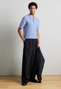 Ανοιχτό μπλε, πλεκτό κοντομάνικο πόλο με υφασμένο διαμάντι μοτίβο, σε συνδυασμό με μαύρο, άνετο παντελόνι και μαύρα παπούτσια.