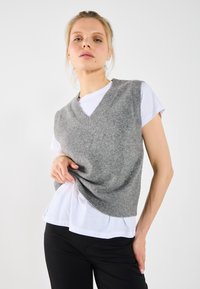 Grå ulltröja med V-ringning, lager på lager över en vit t-shirt. Snygg fit med ribbad kant, tillsammans med svarta byxor.
