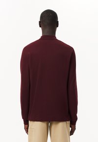 Långärmad polo skjorta i vinröd, tillverkad av mjukt tyg. Har en ribbad krage och mudd, med rak nederkant och minimal detalj.