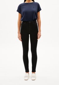 Camiseta de manga corta azul marino, vaqueros pitillo negros de talle alto y zapatos blancos tejidos sin cordones. Diseño simple y moderno.