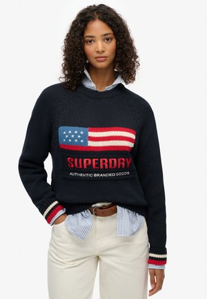 Sudadera de punto azul marino con un diseño texturizado de la bandera americana, acentos en rojo y azul, y el logotipo "SUPERDRY" en el pecho.