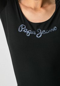 Schwarzes enganliegendes T-Shirt mit Rundhalsausschnitt, das blau gestickten "Pepe Jeans"-Text über der Brust zeigt. Weicher Baumwollstoff.