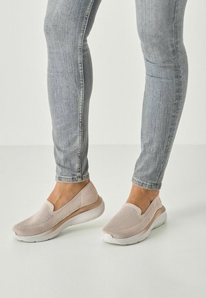 Beige slip-on shoes with a mesh upper and cushioned sole, paired with light blue skinny jeans. Smooth texture and minimal detailing.
