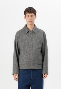 Grå herringbone-jakke med knaplukning, to forlommer og krave. Lavet af tekstureret vævet stof.